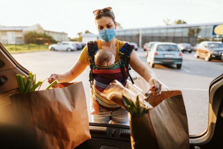 A parent keeping the groceries in the trunk of the car while her baby is strapped to her chest