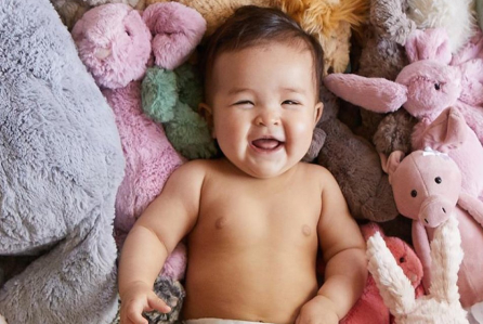 A laughing baby laying on a pile of stuffed animals